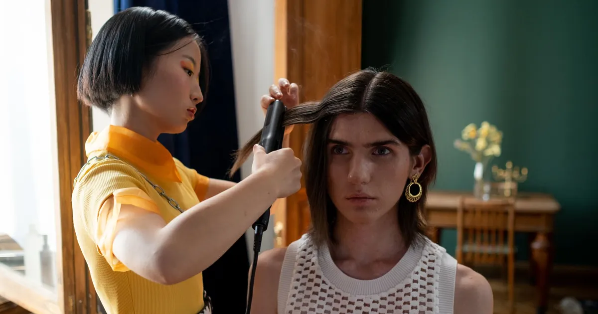Coiffeuse lissant les cheveux d'une cliente au fer dans un salon moderne.