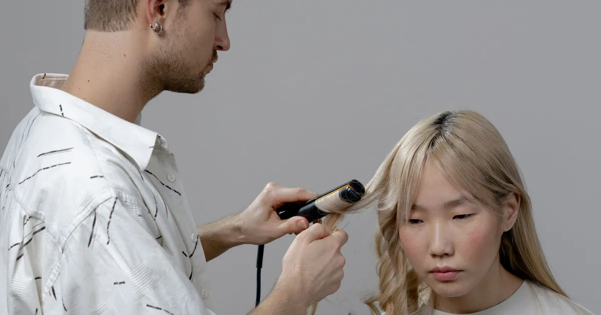 Coiffeuse utilisant un fer à boucler pour coiffer une cliente en salon.
