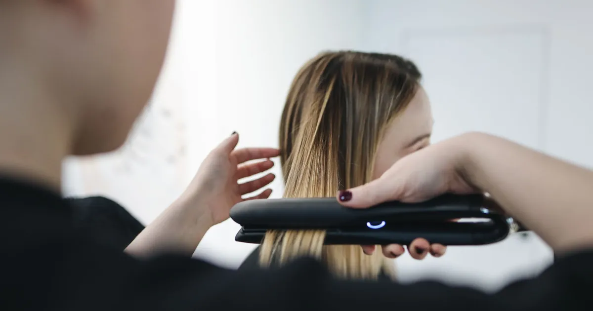 Coiffeur lissant des cheveux au fer plat en intérieur