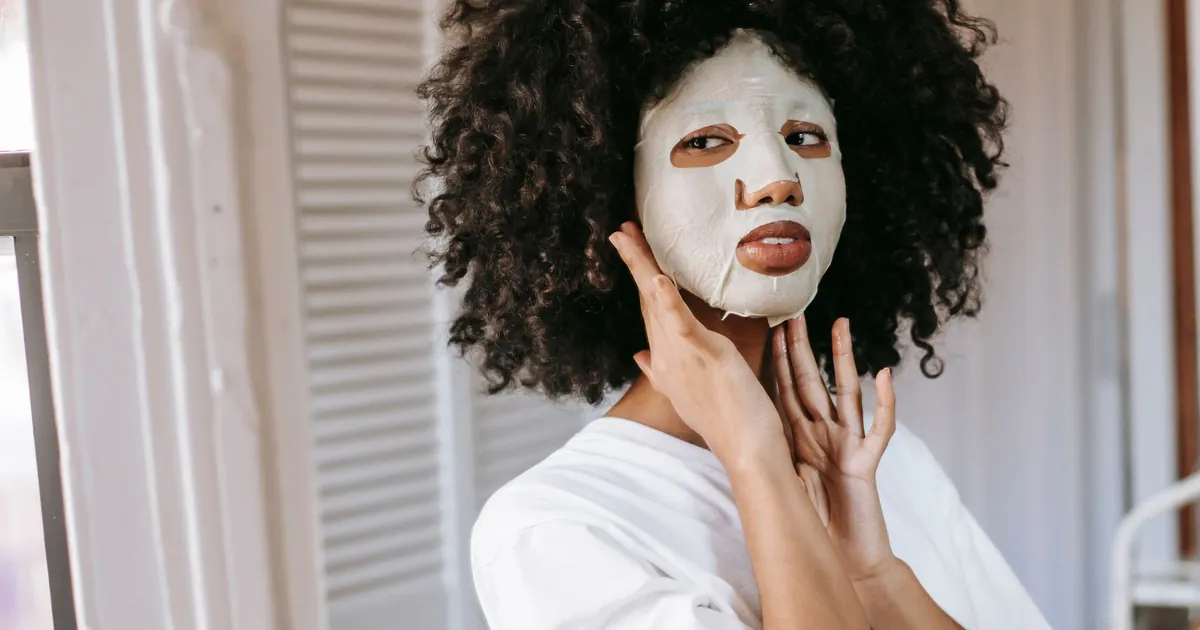 Jeune femme aux cheveux bouclés, masque en tissu blanc, regard détourné.