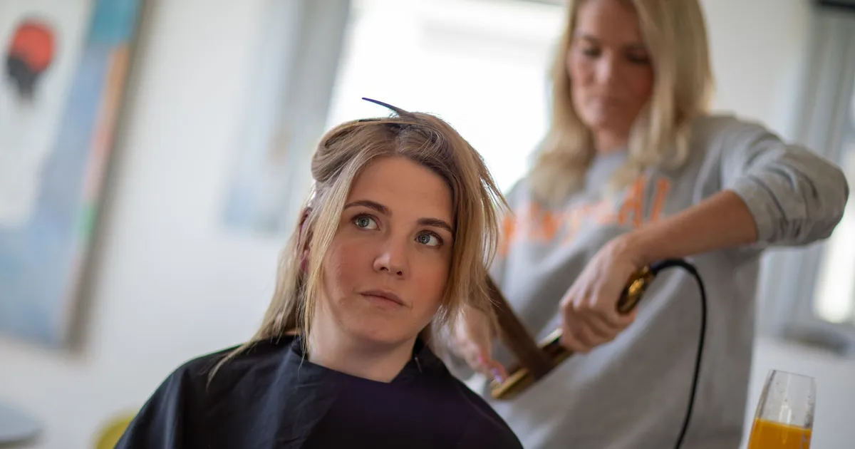 Femme en cape de salon recevant un coiffage professionnel par un coiffeur.