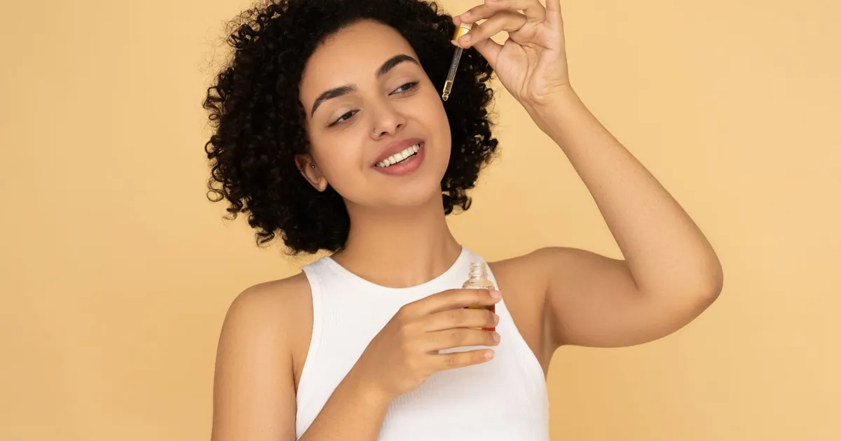 Femme aux cheveux bouclés appliquant une huile essentielle sur sa peau, soin bien-être