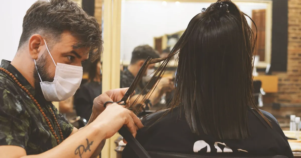 Coiffeur masqué coupant avec soin les cheveux d'une femme en intérieur, ambiance barbier