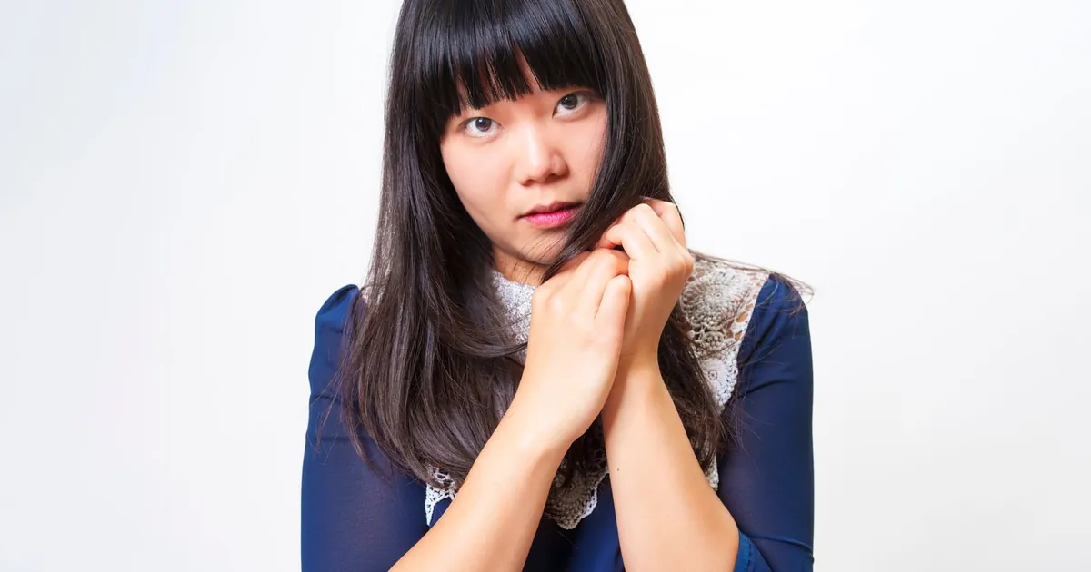 Portrait d'une femme asiatique contemplative tenant ses cheveux sur fond blanc.