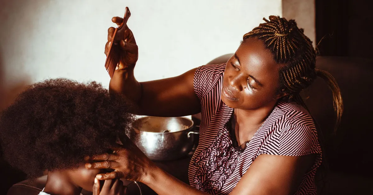 Mère aimante peignant les cheveux afro de son fils à la maison, à Abuja, au Nigeria.