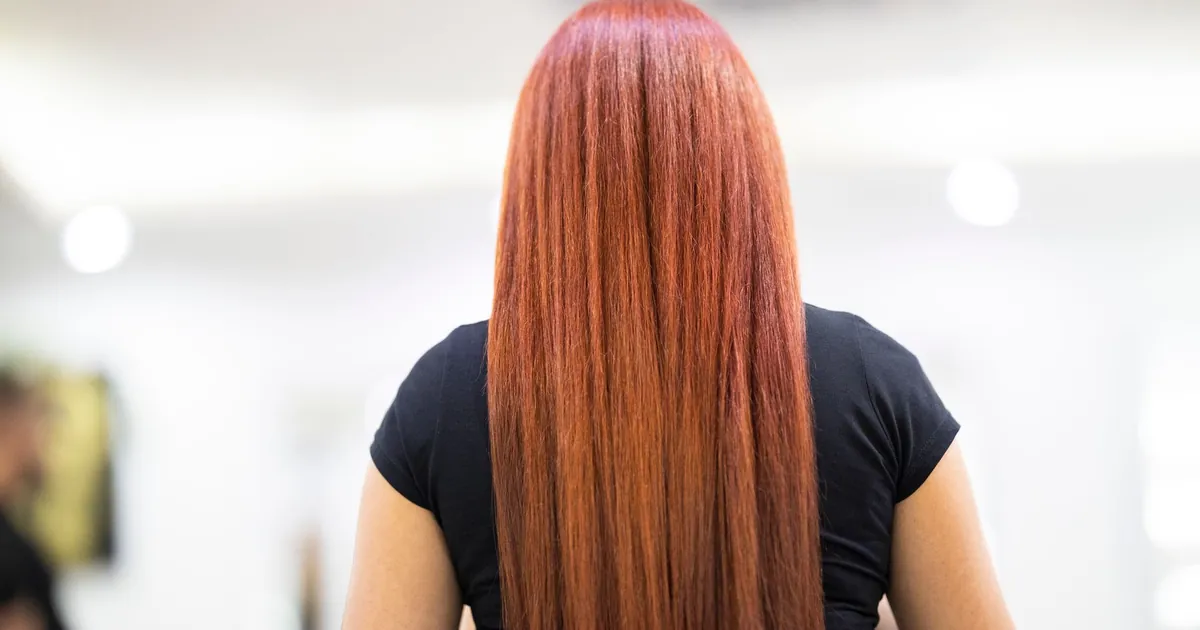 Femme aux cheveux roux lisses vue de dos, coiffure fraîche en salon professionnel.