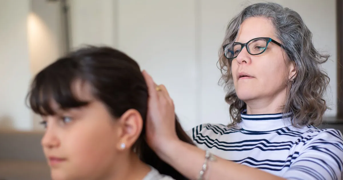 Mère coiffant avec attention les cheveux de sa fille à l'intérieur.