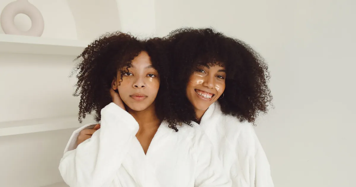 Deux femmes en peignoirs avec patchs visage, se blottissant joyeusement.